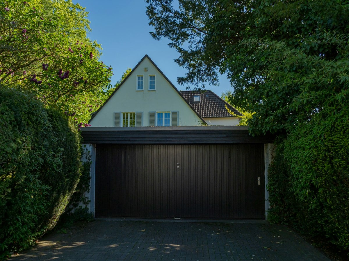 Wide dark garage door on a house behind tall hedges